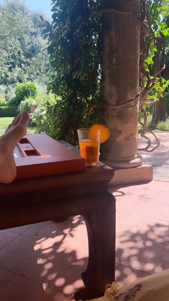 Alice Eve relaxing on outdoor furniture in sunlight.