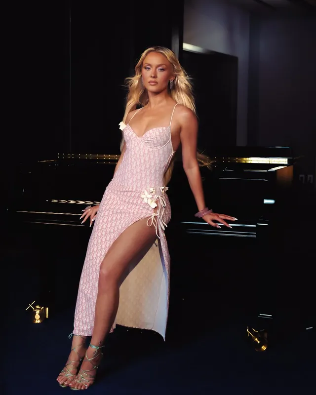 Zara Larsson posing beside a piano in a pink dress and lace-up heels.