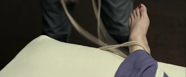 Gemma Arterton lying on a bed in purple trousers in a screen scene.