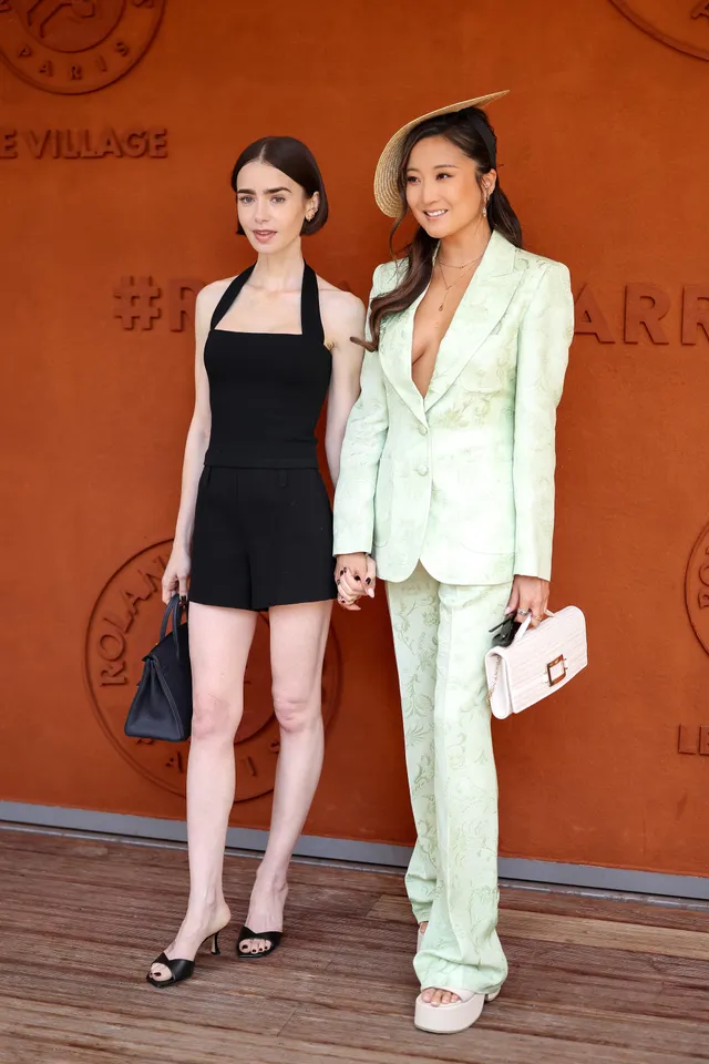 Lily Collins posing with a friend in a black dress and black heels.