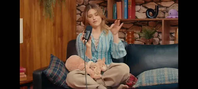 Nicole Wallace speaking into a microphone while sitting barefoot on a sofa.