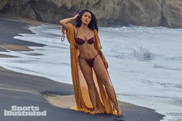 Salma Hayek standing at the edge of the sea in a gold wrap.