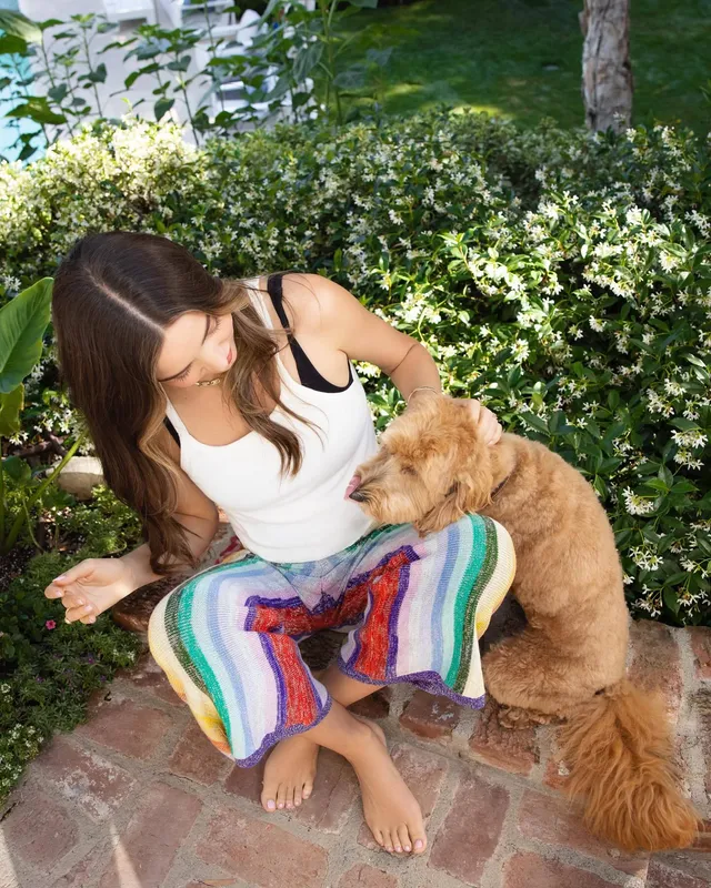 Miranda Kerr crouching barefoot beside a dog in a garden.