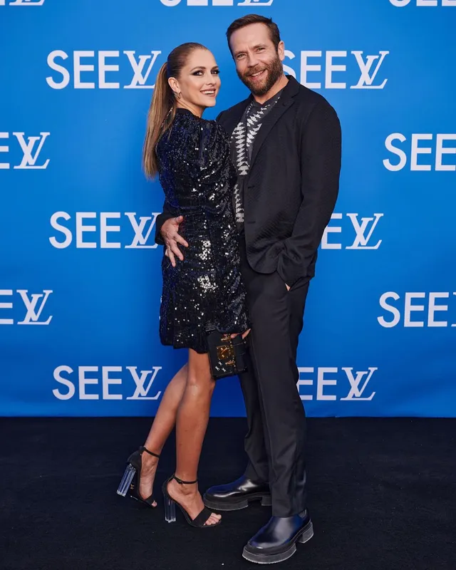 Teresa Palmer posing with a companion against a blue event backdrop.