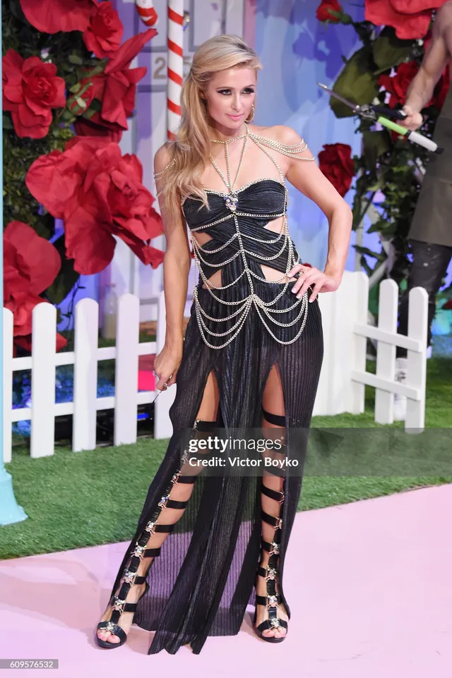 Paris Hilton wearing a black dress and tall strappy sandals at an event.