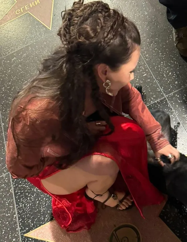 Dafne Keen sitting in a red outfit and black heels.