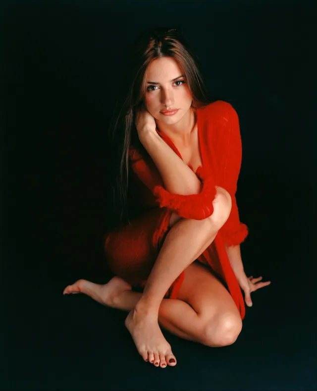 Penélope Cruz crouching against a dark backdrop in a red dress.