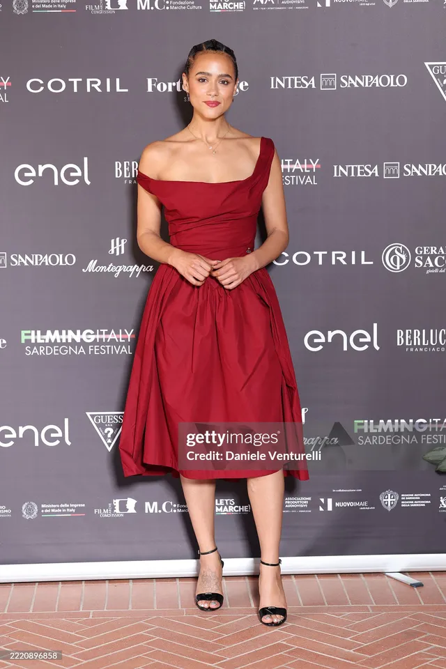 Nathalie Emmanuel posing against a festival backdrop in a red dress.
