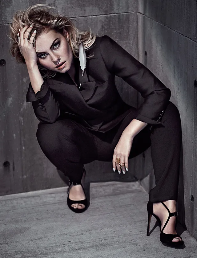 Elisha Cuthbert sitting in a black suit and black heels in a monochrome portrait.