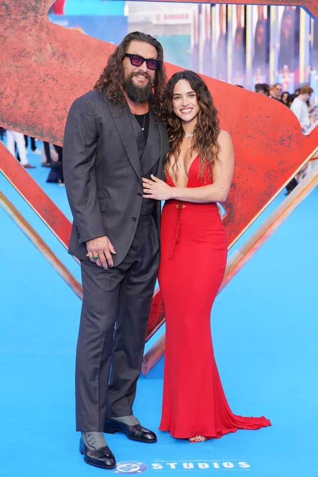 Adria Arjona posing beside a man in a floor-length red gown.