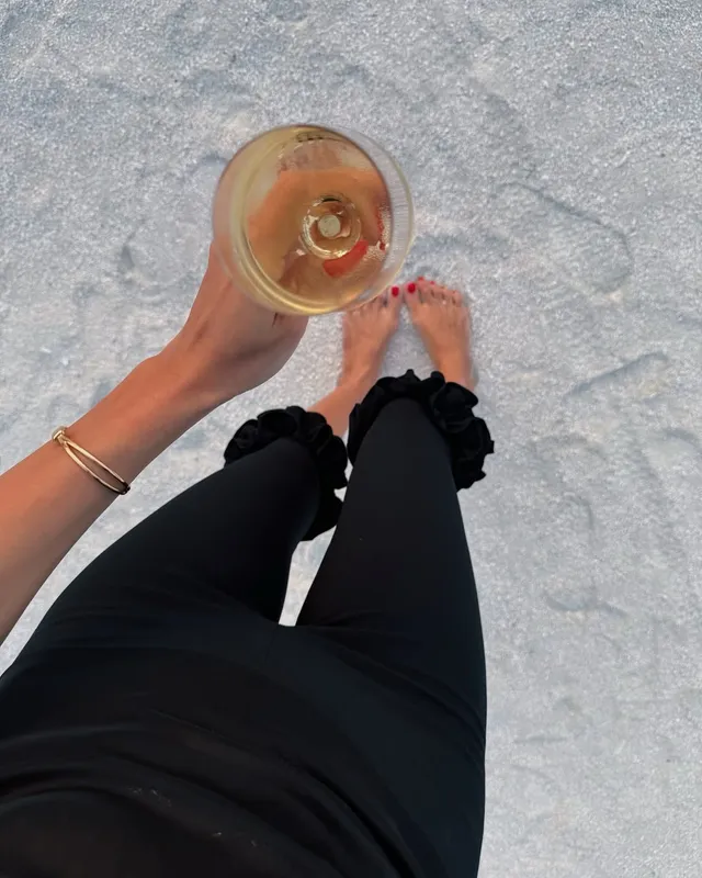 Hande Erçel shown from above with bare feet on a pale surface while holding a glass.