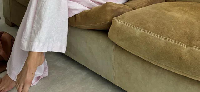 Elsa Hosk wearing pale pointed heels beneath white trousers beside a sofa.