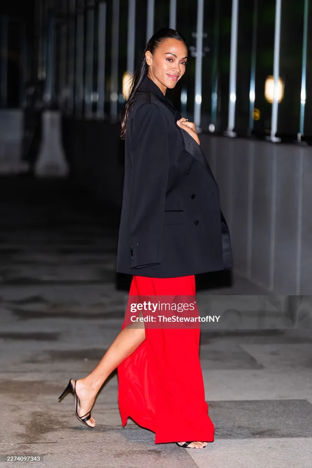 Zoe Saldaña walking in a dark blazer and red skirt.