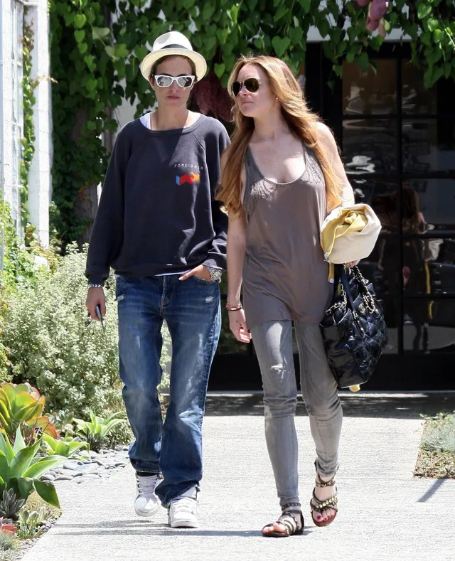 Lindsay Lohan walking outside in a gray outfit and sandals beside a companion.
