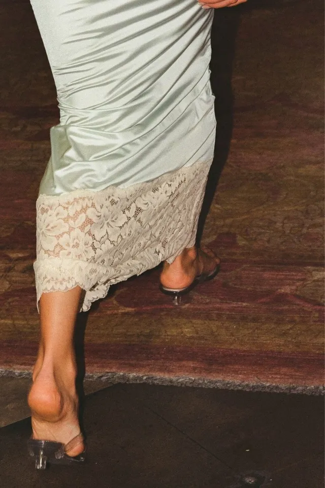 Elsa Hosk wearing clear heeled mules beneath a pale lace-trimmed dress.