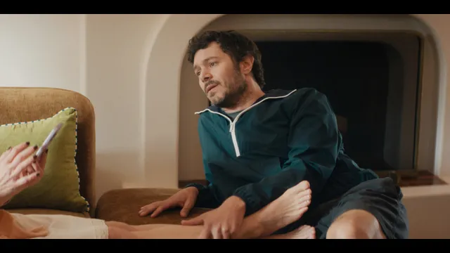 Kristen Bell resting bare feet on a sofa in a television scene.