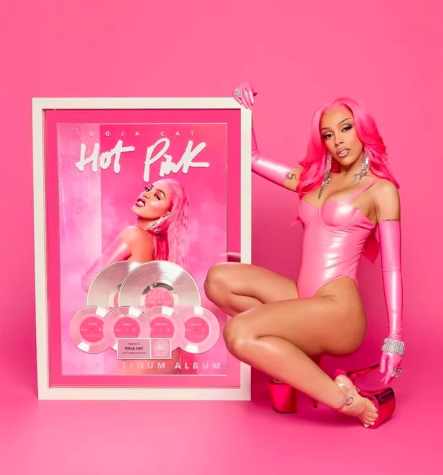 Doja Cat posing in a pink outfit and red platform heels.