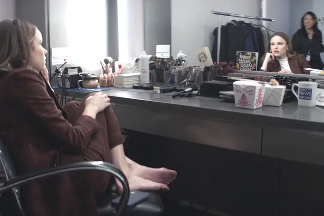 Halston Sage sitting barefoot at a dressing-room table in a scene.