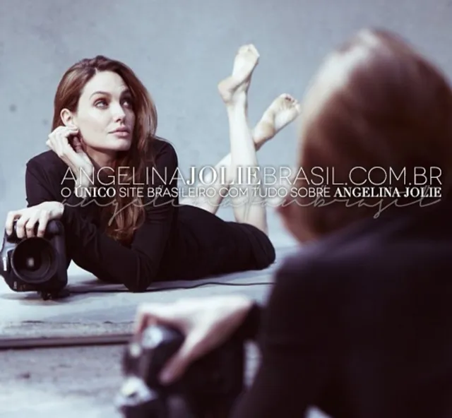 Angelina Jolie lying on the floor with a camera and her feet raised.
