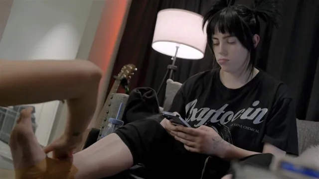Billie Eilish a casual seated photograph using a phone.