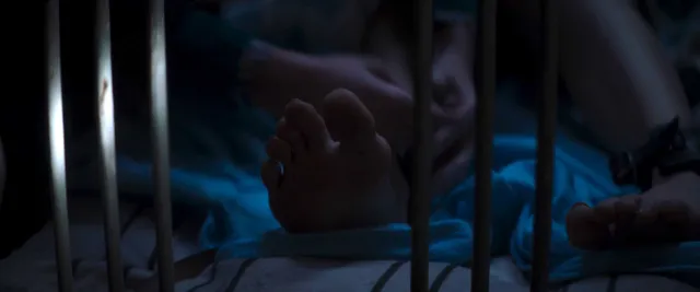 Chloë Grace Moretz with bare soles visible in a dimly lit screen image.