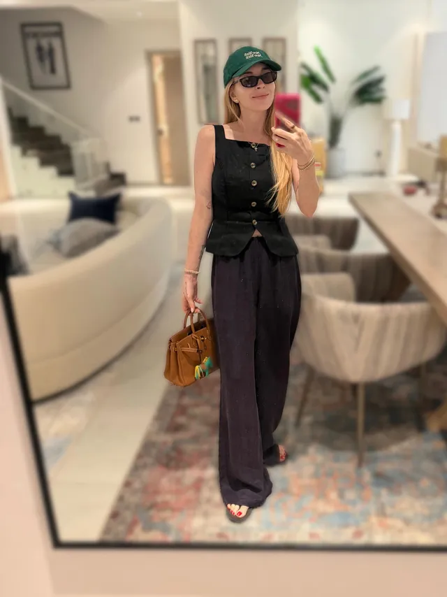 Lindsay Lohan standing indoors in a black outfit for a mirror photograph.