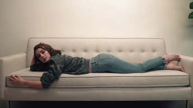 Adelaide Kane lying on a sofa in jeans and a dark top.