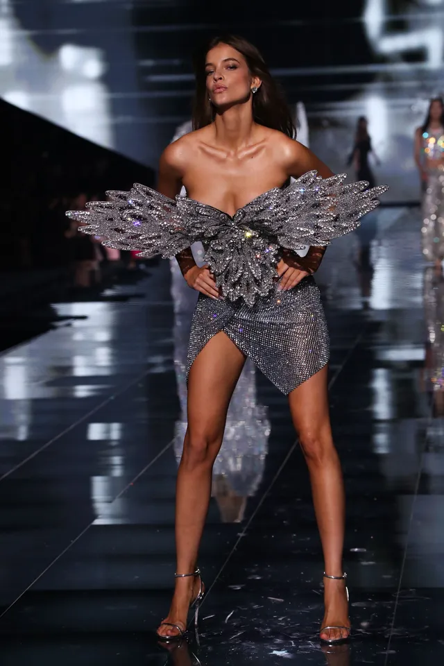 Barbara Palvin walking a runway in a sparkling outfit and heels.