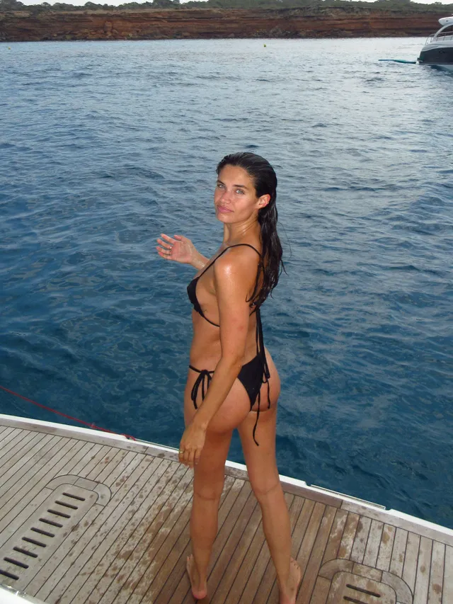 Sara Sampaio standing barefoot on a wooden platform beside the sea.