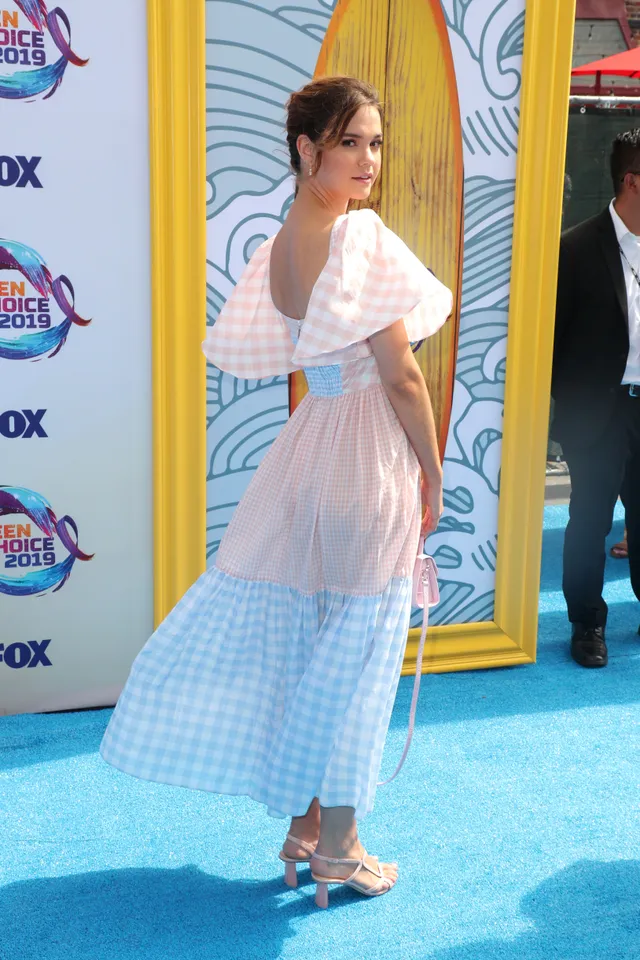 Maia Mitchell turning in a pastel dress and heels on a blue carpet.