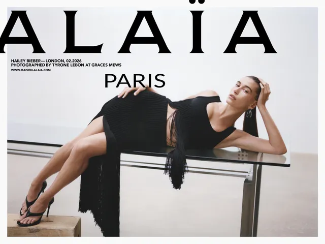 Hailey Bieber reclining in a black dress and sandals in a studio.