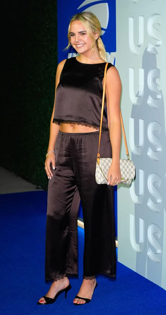 Bailee Madison posing in a dark outfit and black heels.