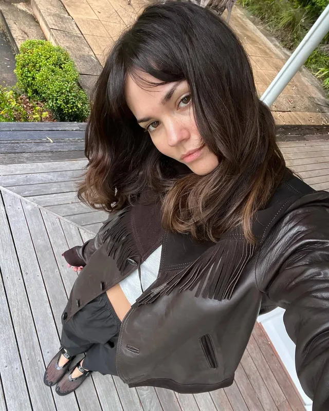 Maia Mitchell taking an outdoor photograph in a black outfit.