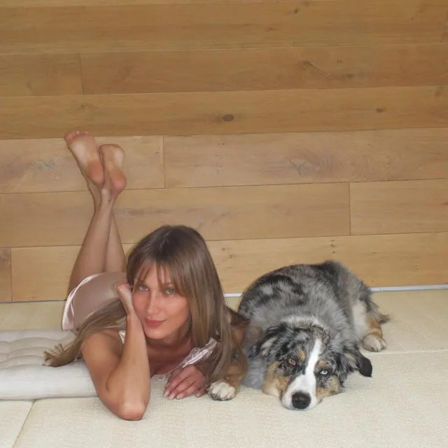 Bella Hadid reclining on a floor with bare soles raised beside a dog.