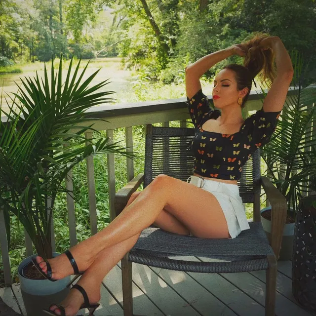Elizabeth Gillies sitting on a balcony chair in a patterned top and shorts.