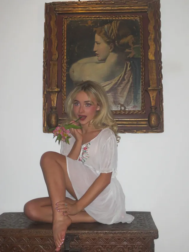 Sabrina Carpenter: seated barefoot beneath a framed portrait.