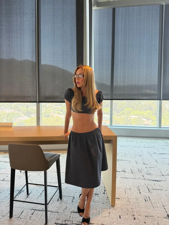 Ester Expósito wearing black heeled mules with a dark skirt and short top during a screen scene.