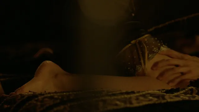 Eva Green lying on patterned bedding in a dim film scene.
