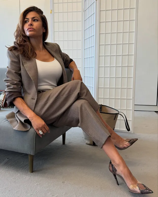 Eva Mendes sitting in a chair in a tailored grey suit.