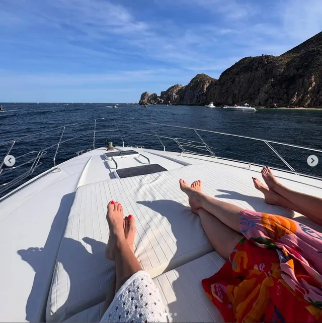 Alex Morgan resting her bare feet on a boat deck beside companions.