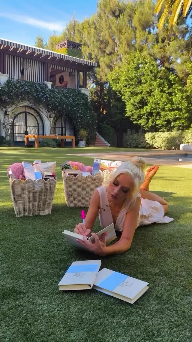 Christina Aguilera lying on grass beside open books with her bare soles raised.