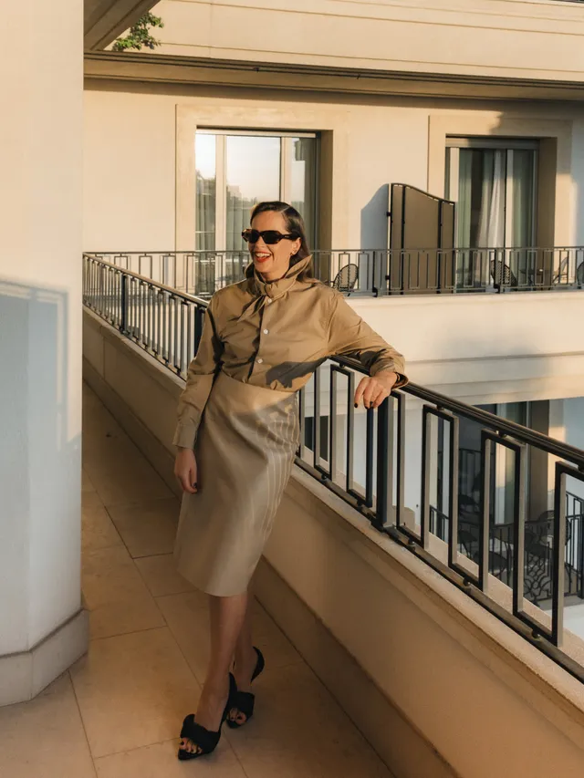 Felicity Jones standing on a balcony in a beige skirt and black mules.