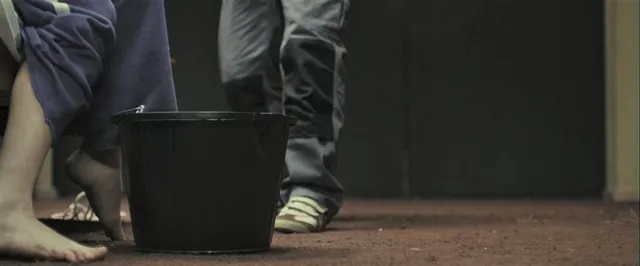 Gemma Arterton standing beside a bucket in a screen scene.