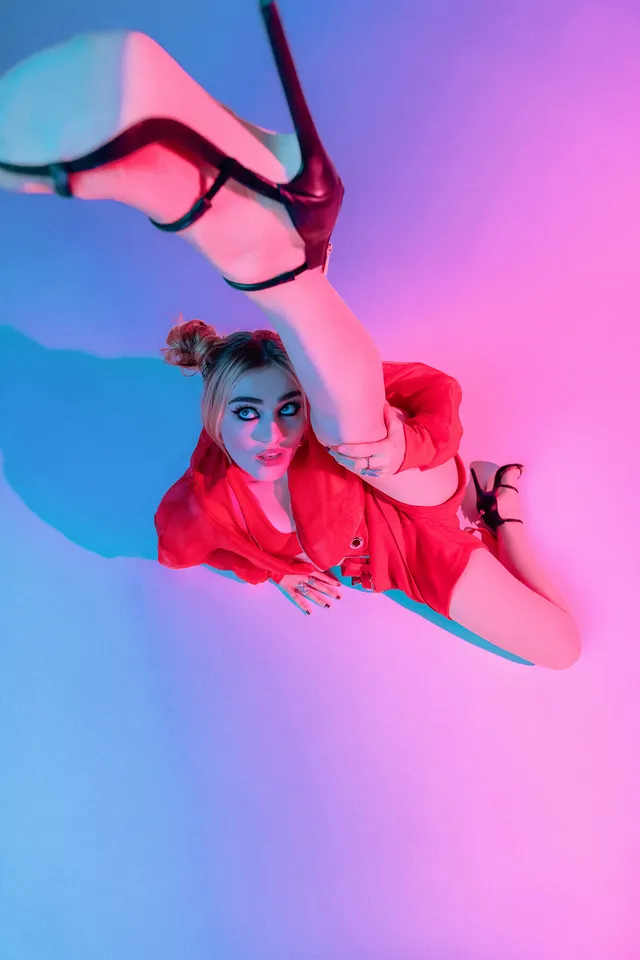 Meg Donnelly reclining in a red outfit with one black heel raised in a studio.