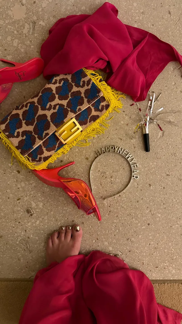 Lily Allen showing a bare foot beside a patterned handbag on a beach.