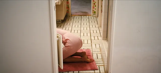 Sydney Sweeney resting barefoot on a bathroom floor in a film scene.