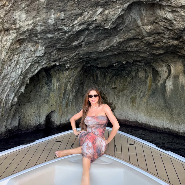 Sofía Vergara standing barefoot on a boat inside a rocky cove.