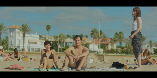 Úrsula Corberó standing barefoot beside fellow performers on a beach.