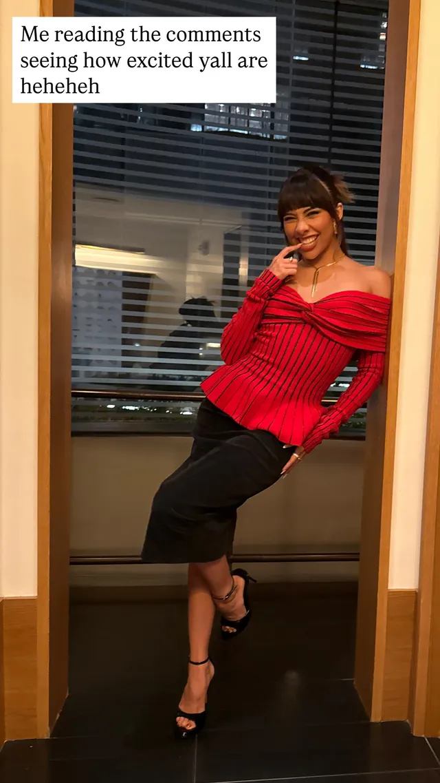 Xochitl Gomez standing against a mirror in a red top and black heels.