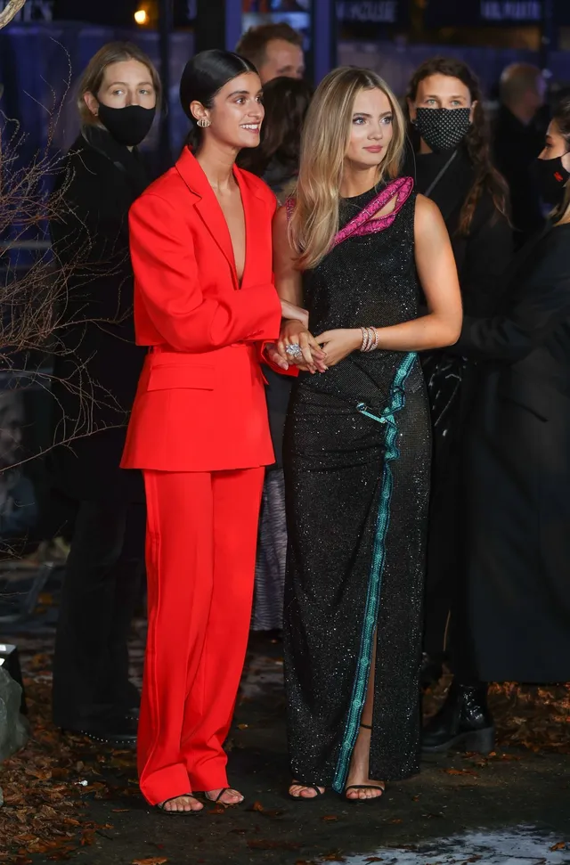 Anya Chalotra posing beside another woman in a red suit and heels.